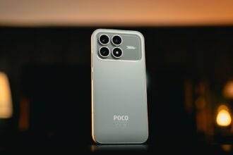 Smartphone in grüner Farbe liegt auf einem Stapel aus wiederverwendbaren Materialien wie Holz und Stoff, umgeben von einer nachhaltigen Lebensweise.